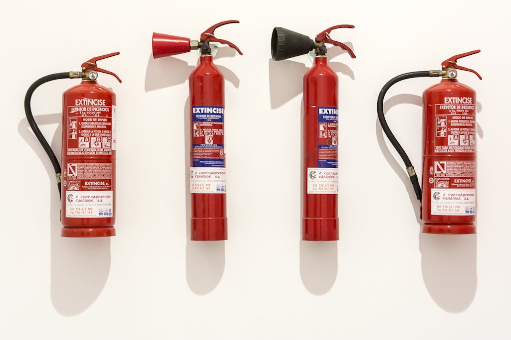Four red fire extinguishers hanging on a clean white wall in an orderly fashion.