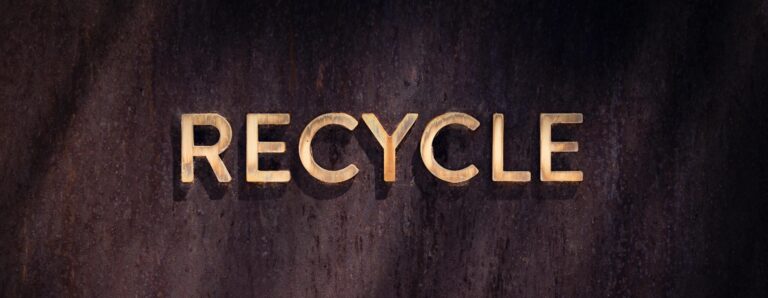 Golden "Recycle" sign on a rustic wood wall, highlighting eco-friendly concepts.