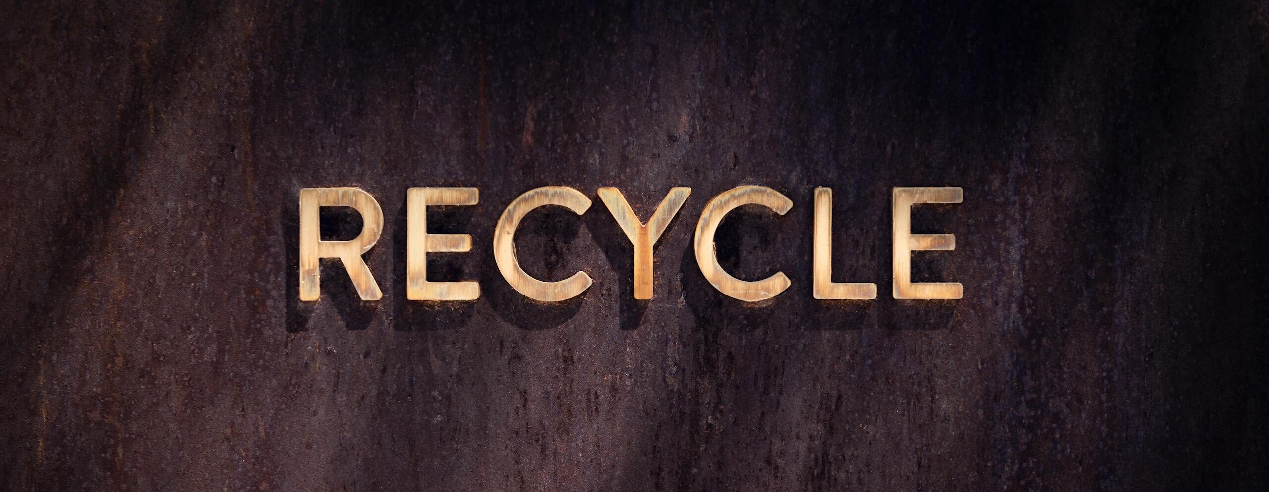 Golden "Recycle" sign on a rustic wood wall, highlighting eco-friendly concepts.